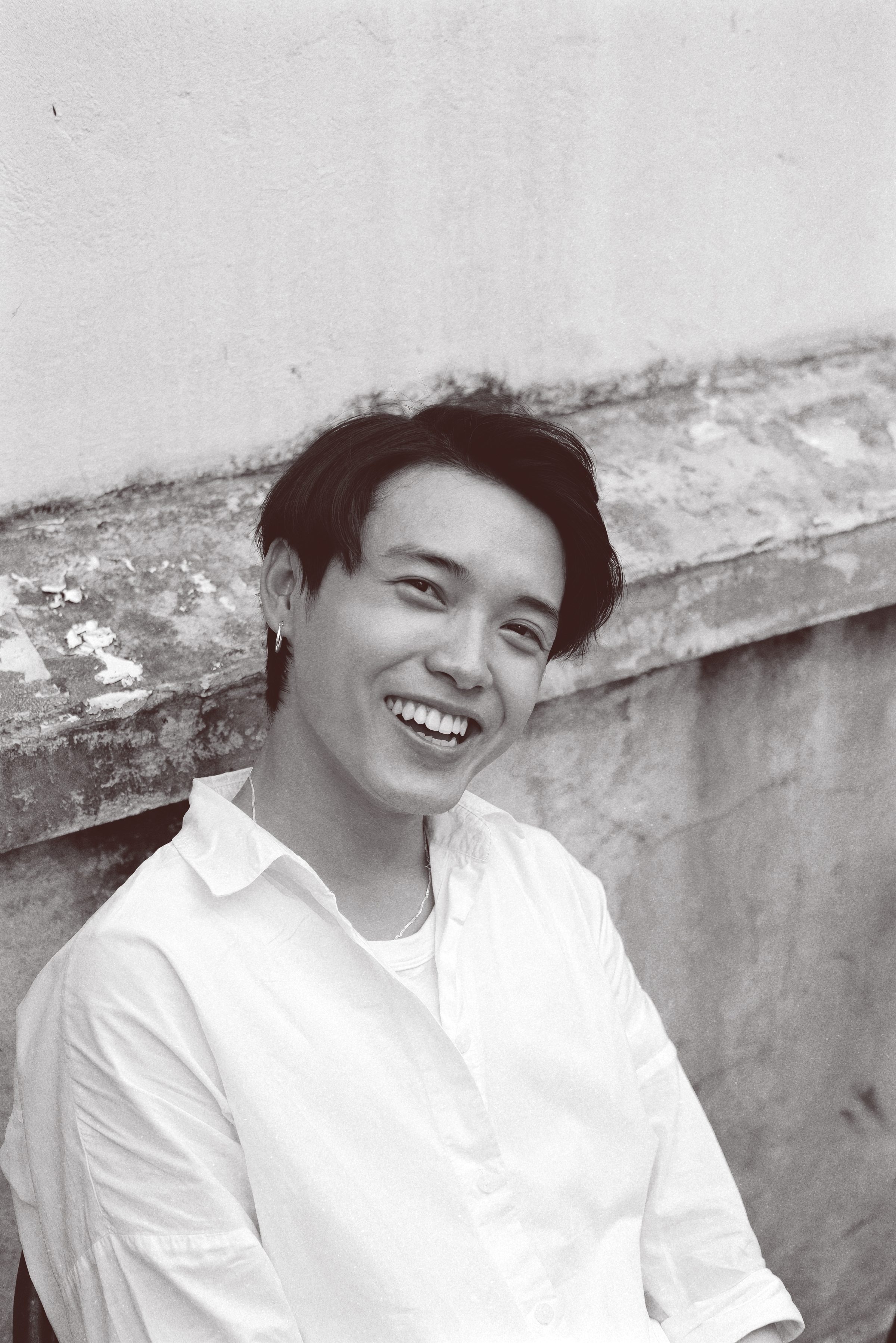 Black-and-white portrait of a young man laughing as he leans against a textured wall