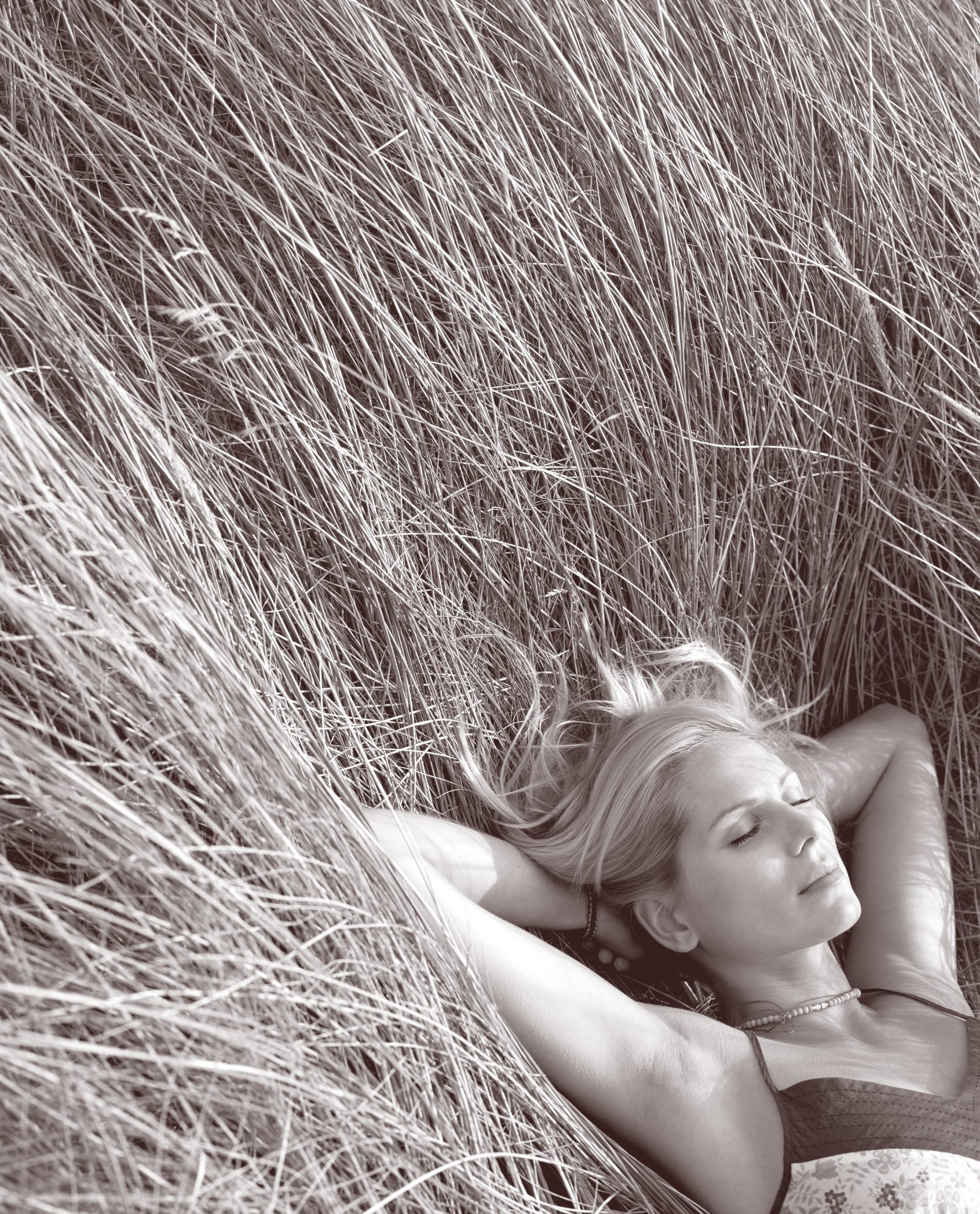 Black-and-white high-angle photograph of a woman with fair hair lying at rest in tall grass
