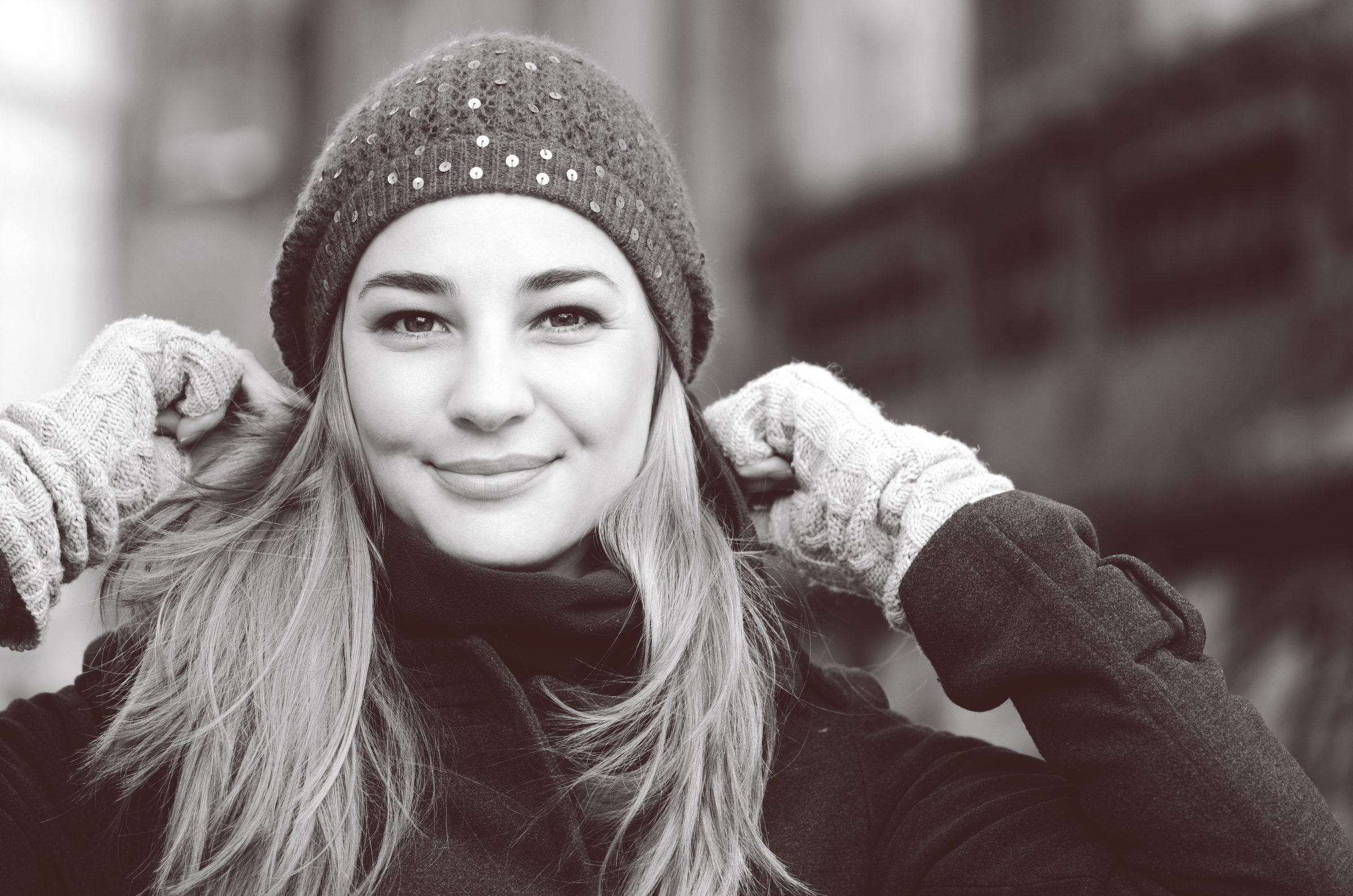 Black-and-white portrait of a smiling woman in a knitted winter hat and gloves